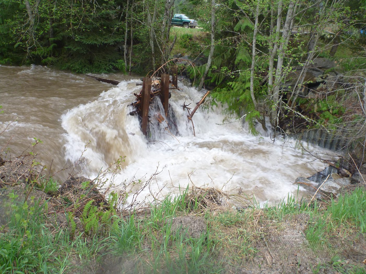 A creek in flood pouring over a damaged weir